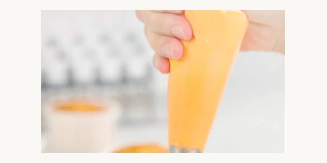 Orange buttercream being piped from a bag, coloured with high-concentration food coloring