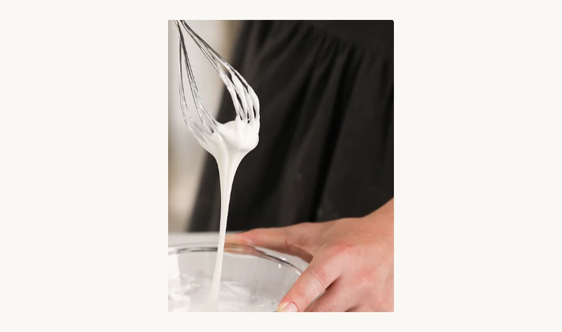Royal icing whipped to a stiff peak from pre-mix powder, held on a whisk over a glass bowl